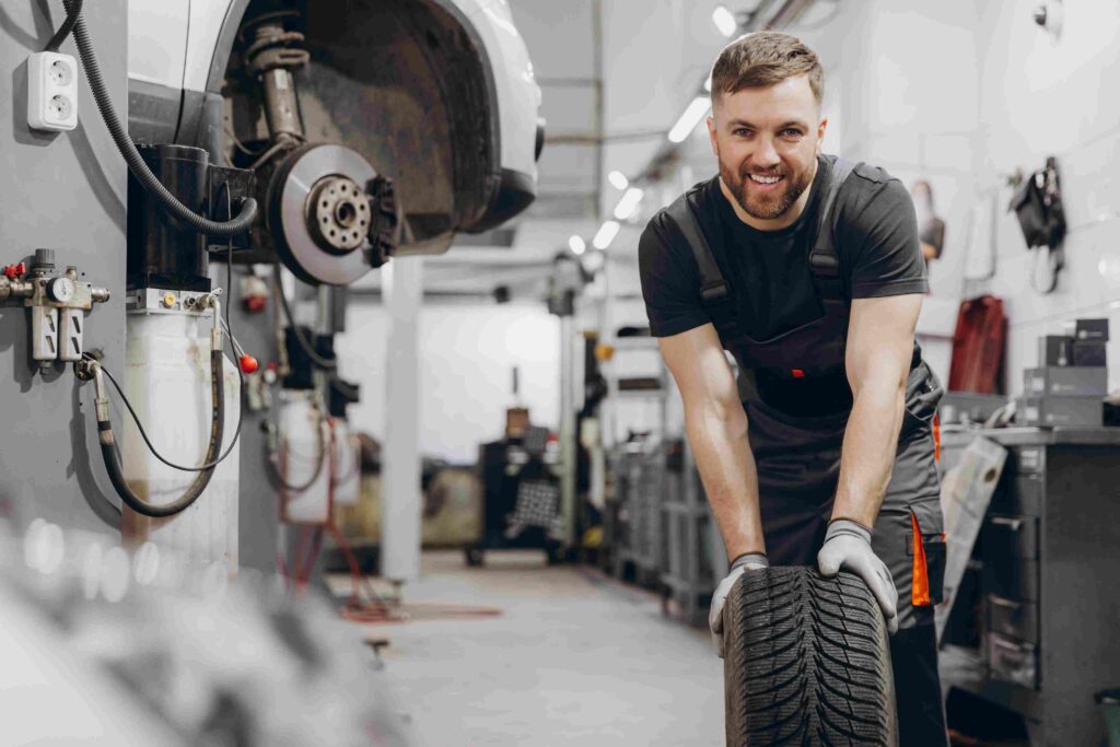Ein KFZ-Mechatroniker aus dem Ausland in schwarzer Arbeitskleidung wechselt einen Reifen in einer modernen Autowerkstatt.